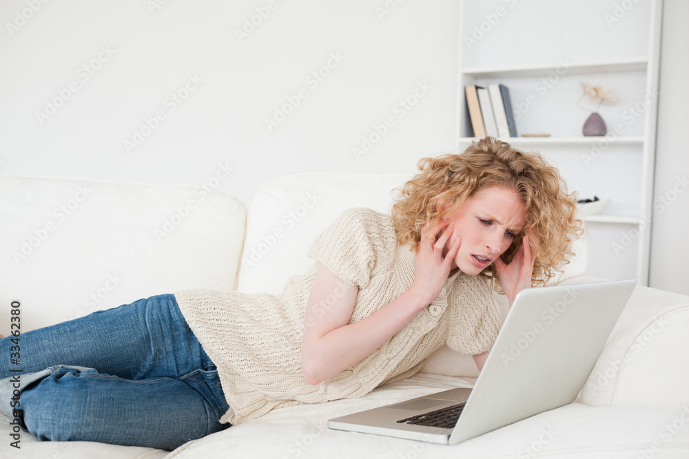 Gorgeous blonde woman relaxing with her laptop while lying on a Gorgeous blonde woman relaxing with her laptop while lying on a