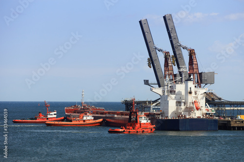 Tug boats pushing a cargo ship to port.