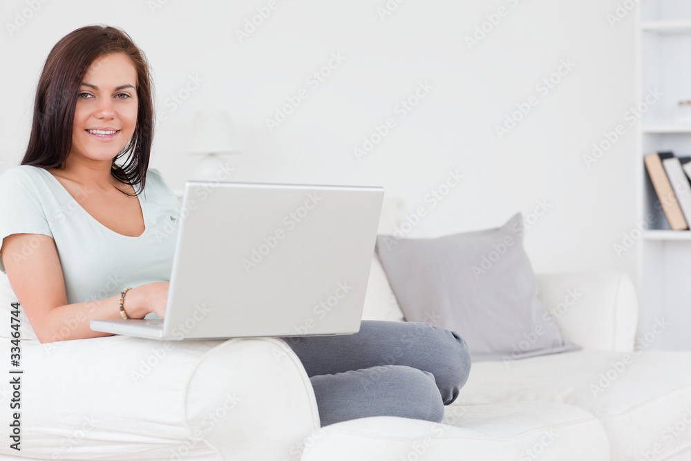 Close up of a charming brunette sitting on a sofa using a laptop Close up of a charming brunette sitting on a sofa using a laptop