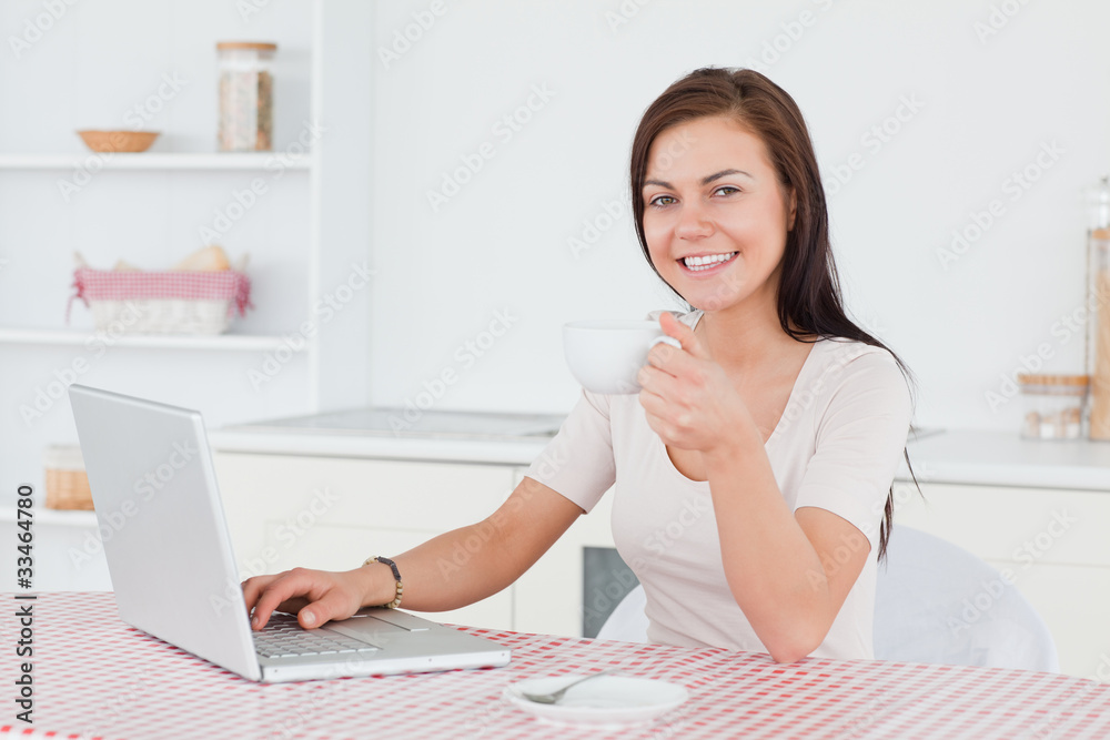 Charming brunette using her laptop and having a tea Charming brunette using her laptop and having a tea