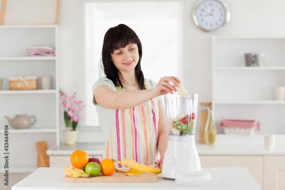 Gorgeous brunette woman putting vegetables in a mixer while stan