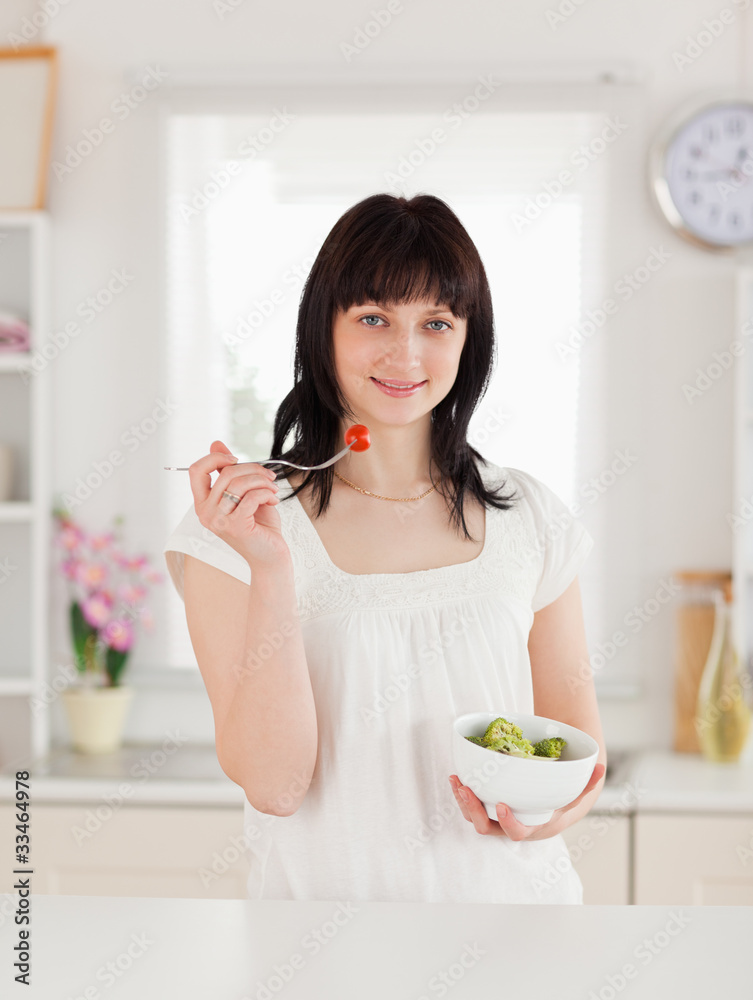 Cute brunette female eating a cherry tomato while holding a bowl Cute brunette female eating a cherry tomato while holding a bowl