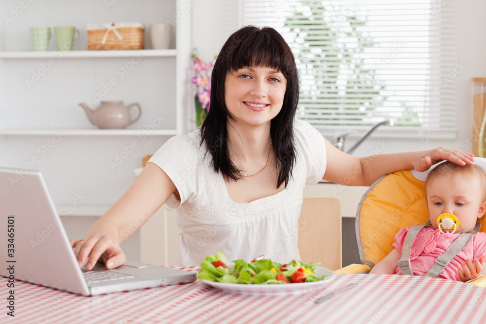 Attractive brunette woman eating a salad next to her baby while