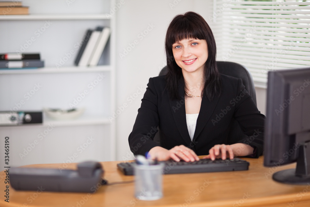 Pretty brunette woman working on a computer while sitting at a d Pretty brunette woman working on a computer while sitting at a d