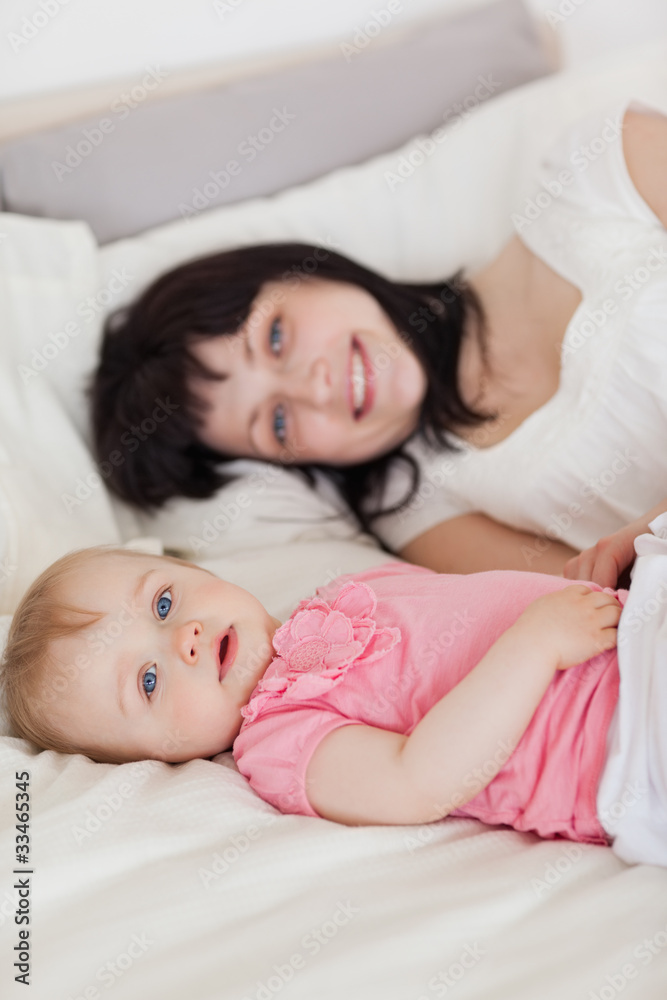 Attractive brunette female posing with her baby while lying on a Attractive brunette female posing with her baby while lying on a