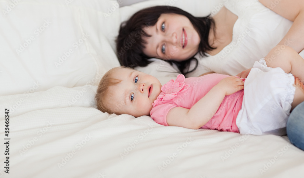 Beautiful brunette female posing with her baby while lying on a Beautiful brunette female posing with her baby while lying on a
