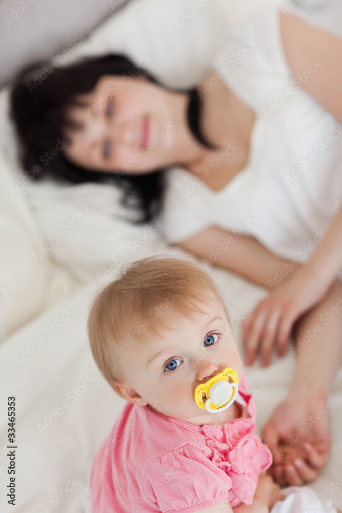 Cute baby looking at the camera while her mother is lying on a b Cute baby looking at the camera while her mother is lying on a b