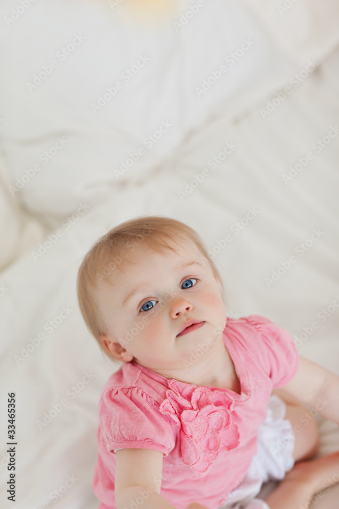 Cute baby looking at the camera while sitting on a bed Cute baby looking at the camera while sitting on a bed