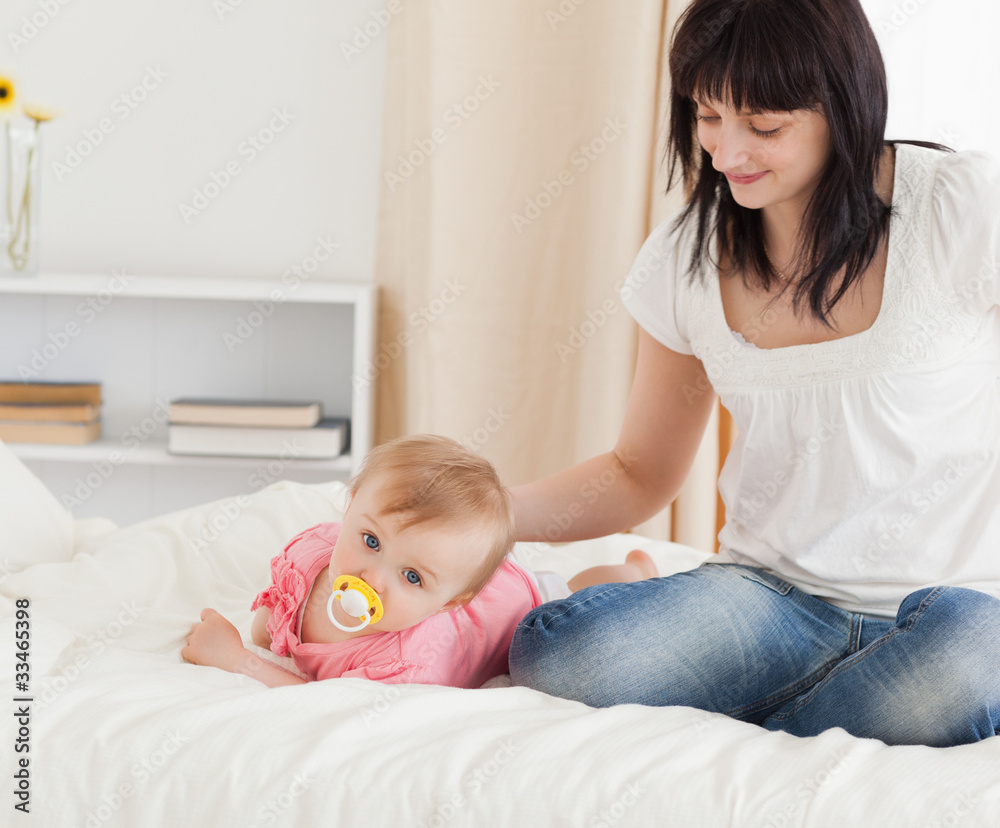 Cute brunette woman looking at her lying baby on a bed Cute brunette woman looking at her lying baby on a bed