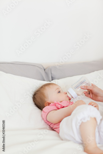 Female hand bottle-feeding her baby on a bed