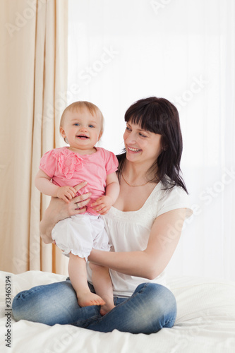 Cute brunette woman holding her baby on her knees while sitting © WavebreakmediaMicro