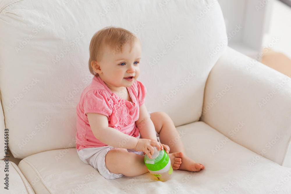 Blond baby playing with a ball while sitting on a sofa Blond baby playing with a ball while sitting on a sofa