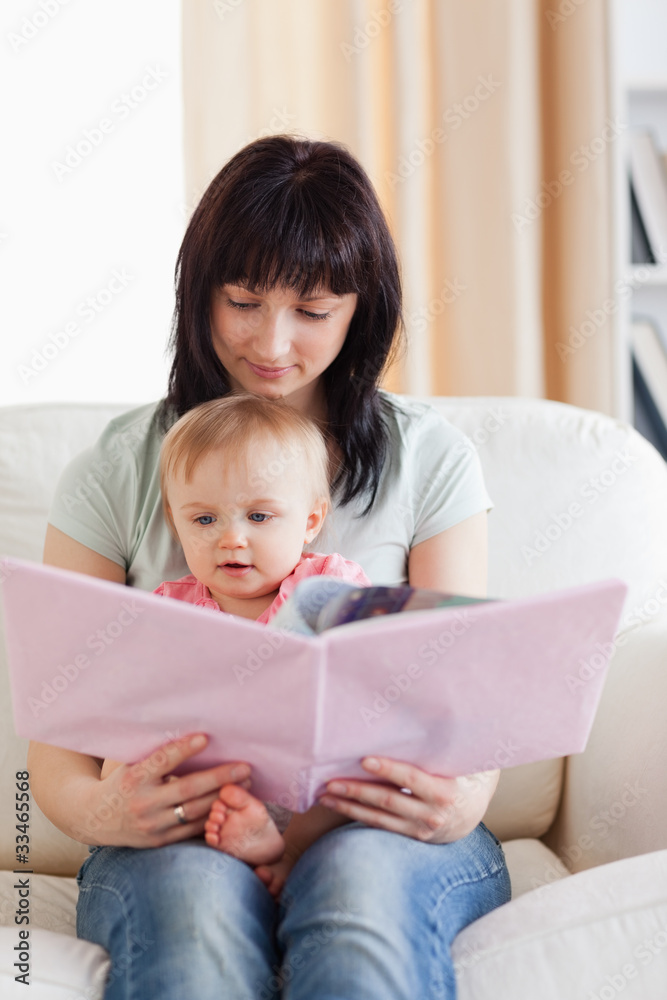 Pretty woman holding her baby and a book in her arms while sitti Pretty woman holding her baby and a book in her arms while sitti