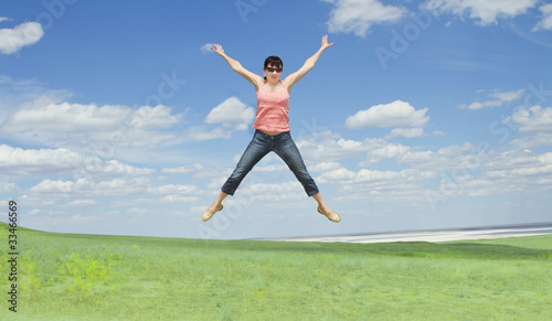 pretty young woman jumping on green grass over blue sky © Aleksandr Kurganov