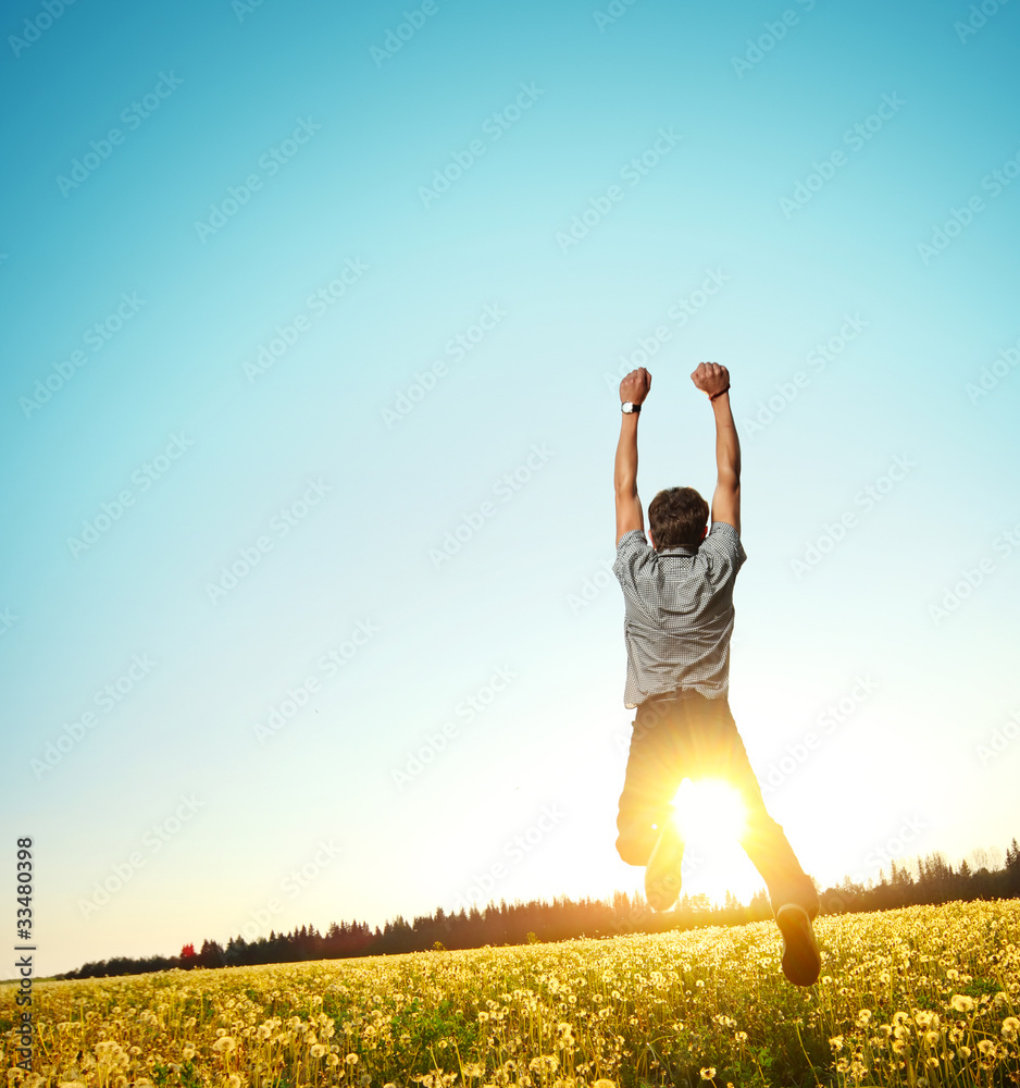 Fototapeta premium Young man jumping on meadow with dandelions on cloudy background