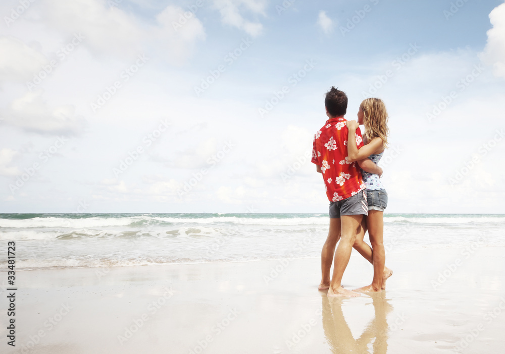 Young couple standing on wet sand by sea and looking to a blue sky