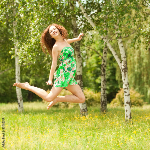 Young redhead woman jumping in the park with flowers
