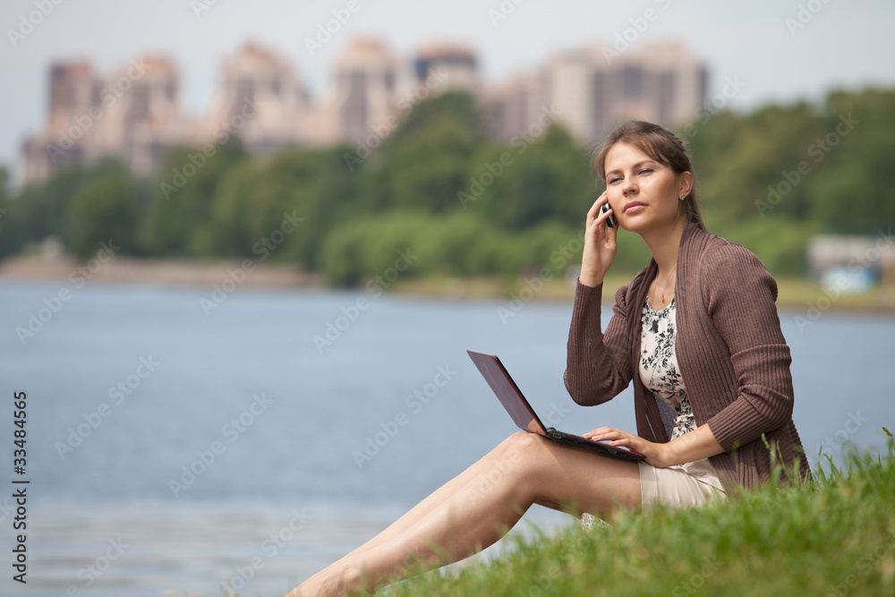 Young woman with laptop and mobile phone in the park.
