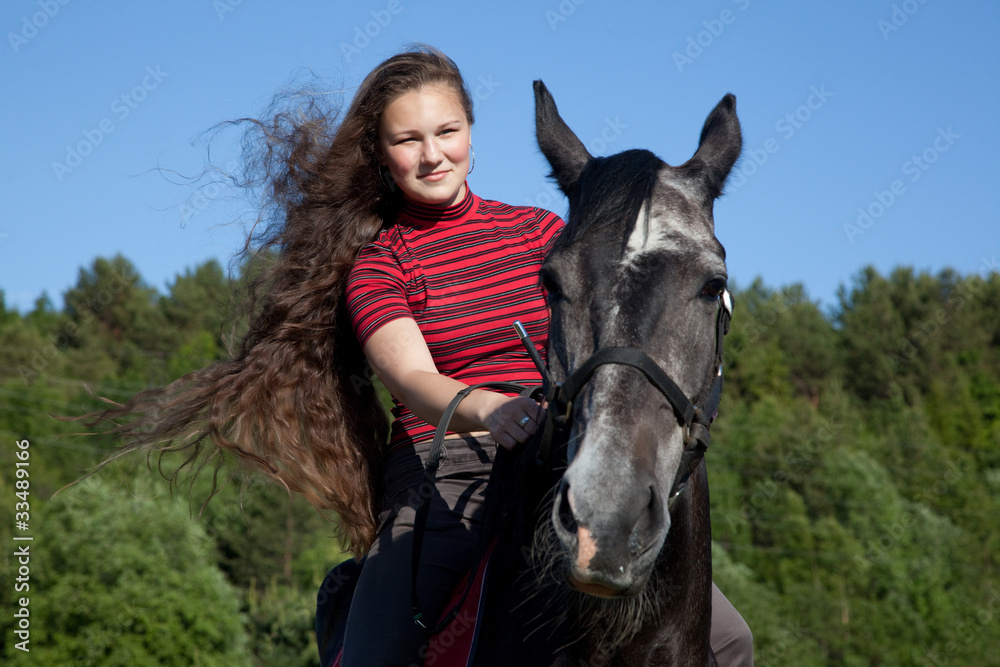 Obraz premium Beautiful girl with brown hair on a black horse