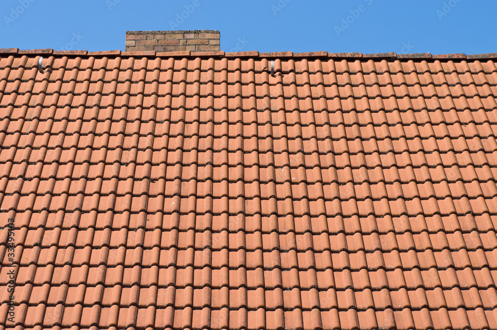 The roof of tiles and chimney against a blue sky.