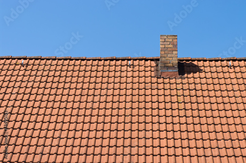 The roof of tiles and chimney against a blue sky.