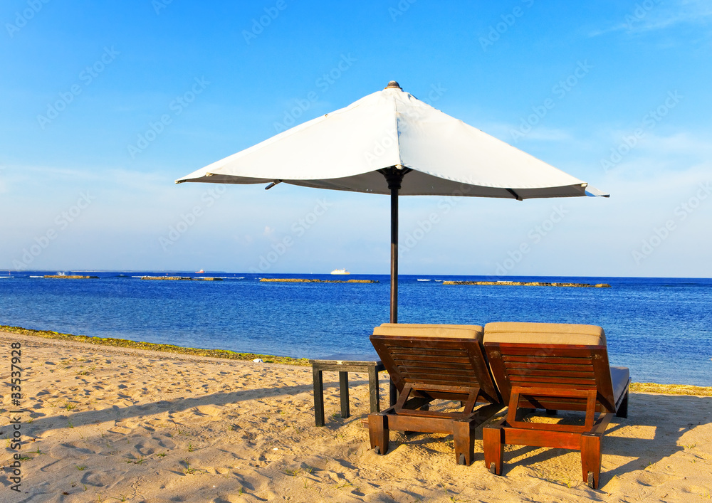 Umbrella and chaise lounges on a beach.