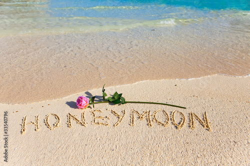 On sand an inscription "Honeymoon" and a blossoming rose..