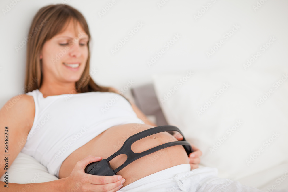 Attractive pregnant woman using headphones while lying on a bed Attractive pregnant woman using headphones while lying on a bed