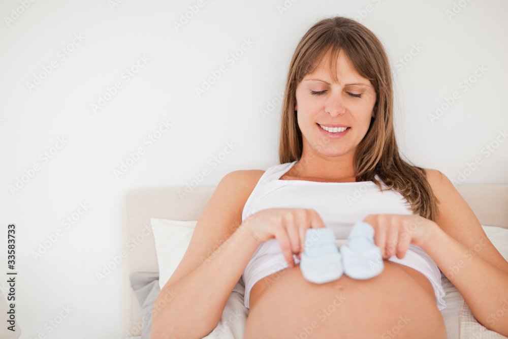 Lovely pregnant woman playing with little socks while lying on a Lovely pregnant woman playing with little socks while lying on a
