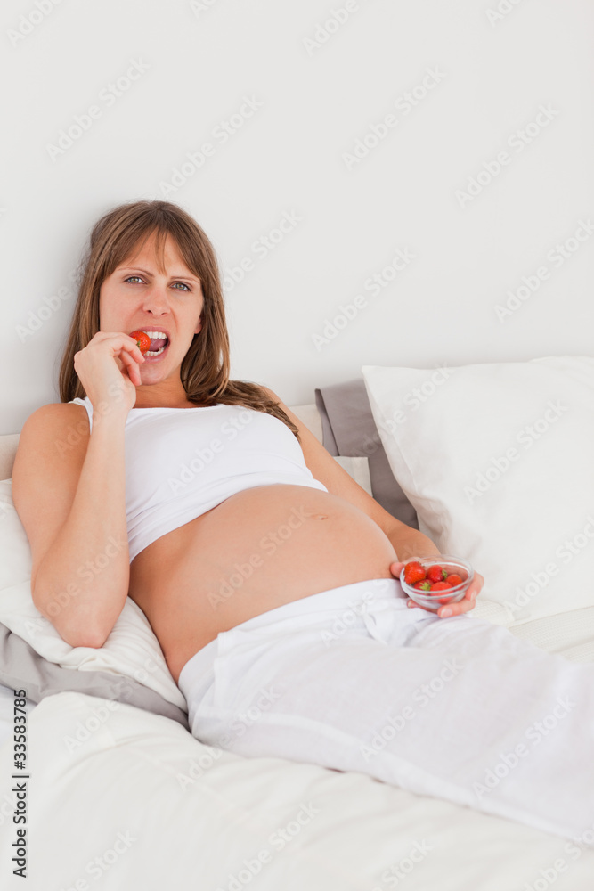 Good looking pregnant female eating some strawberries while lyin Good looking pregnant female eating some strawberries while lyin