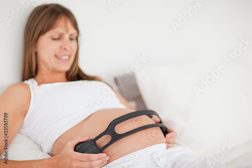 Attractive pregnant woman using headphones while lying on a bed