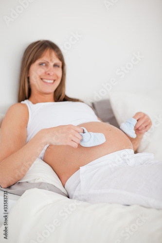 Charming pregnant woman playing with little socks while lying on