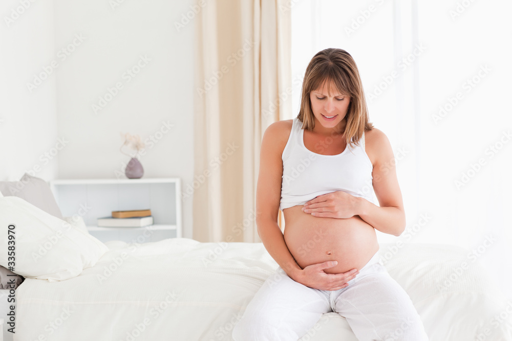 Attractive pregnant female caressing her belly while sitting on Attractive pregnant female caressing her belly while sitting on