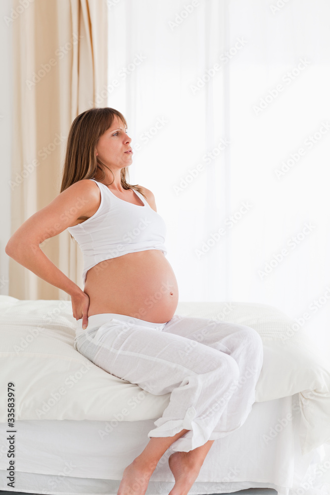 Good looking pregnant female having a back pain while sitting on Good looking pregnant female having a back pain while sitting on