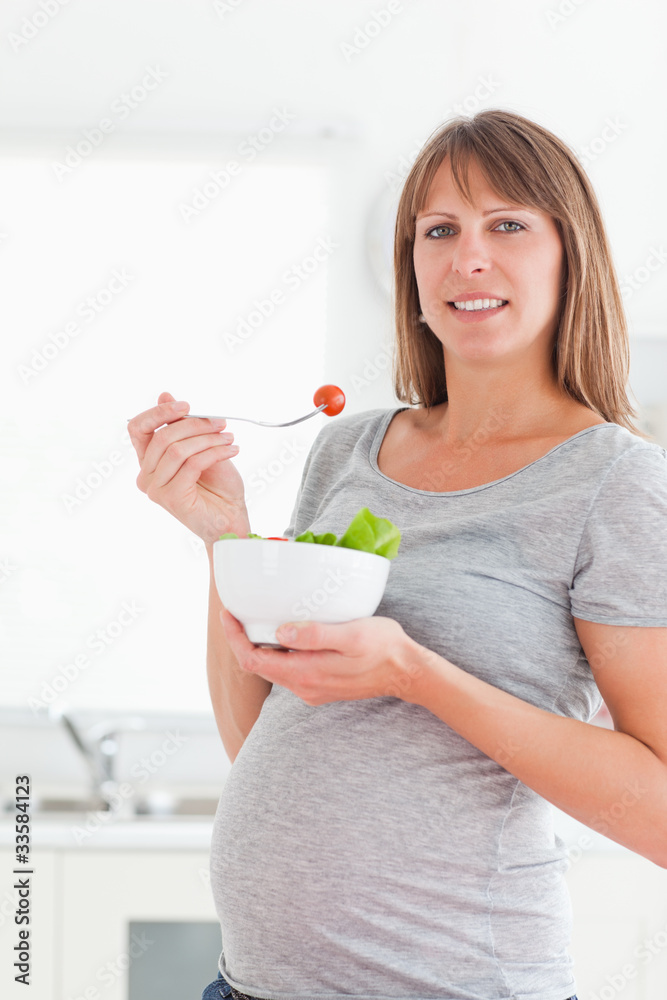 Pretty pregnant woman eating a cherry tomato while standing
