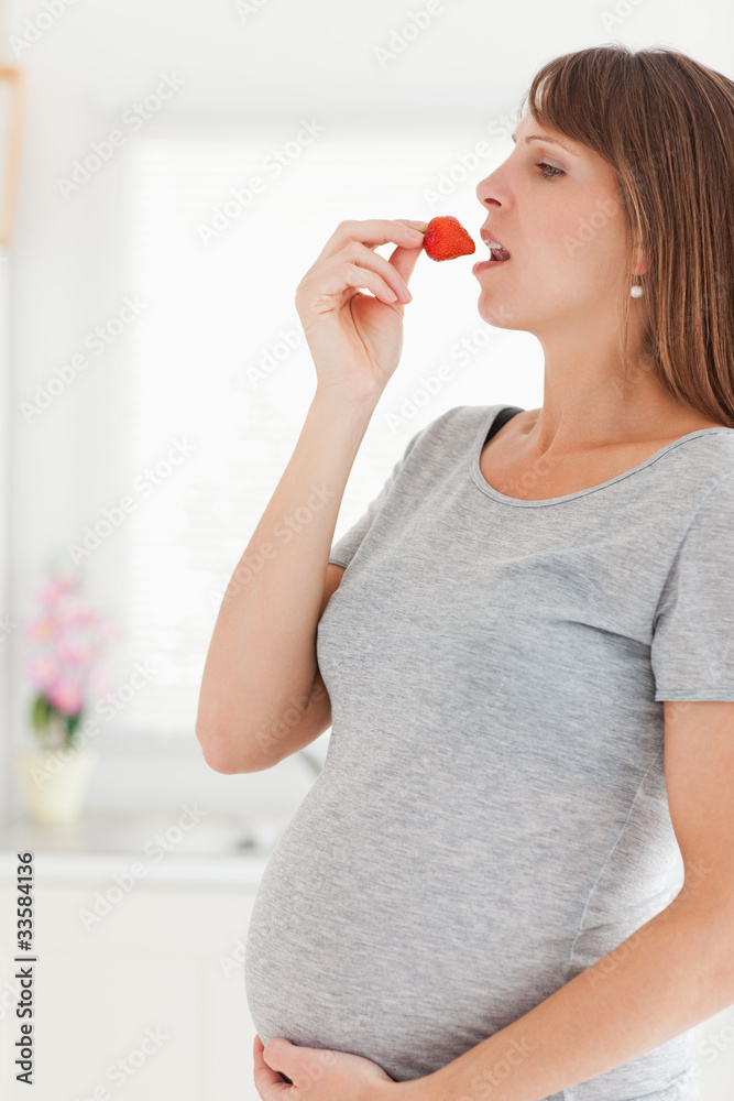 Pretty pregnant woman eating a strawberry while standing Pretty pregnant woman eating a strawberry while standing