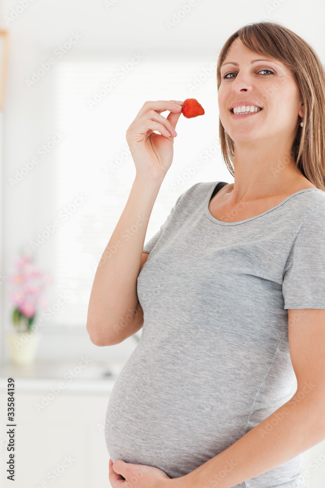 Beautiful pregnant woman eating a strawberry while standing Beautiful pregnant woman eating a strawberry while standing
