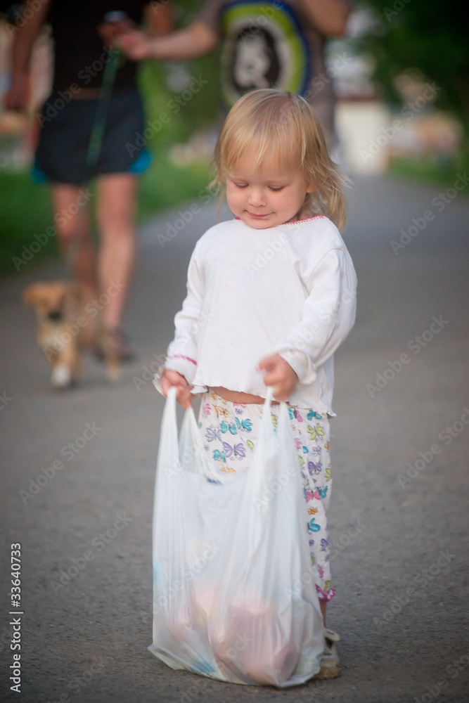 Adorable toddler girl draggin bag with food from supermarket by Adorable toddler girl draggin bag with food from supermarket by