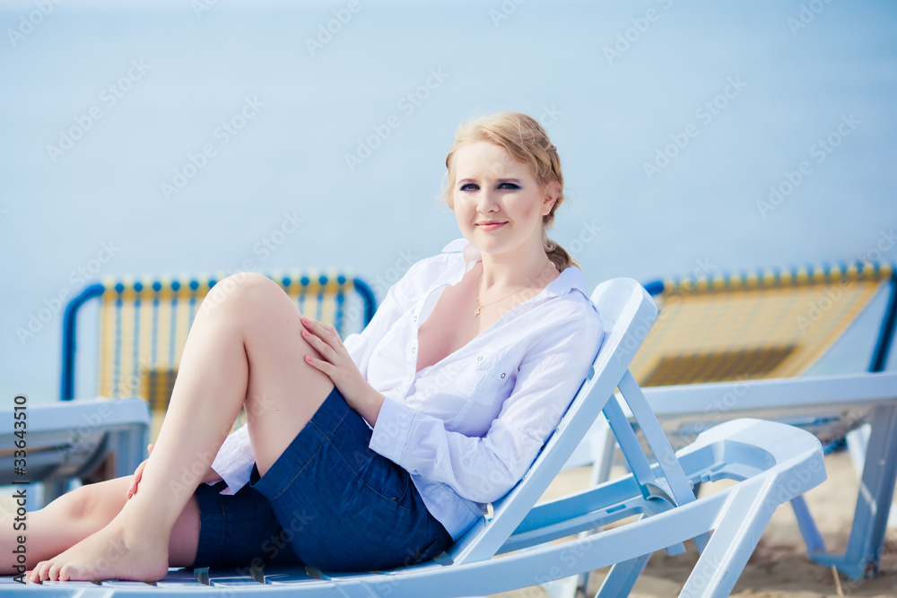 Beautiful woman sitting in chaise on the beach