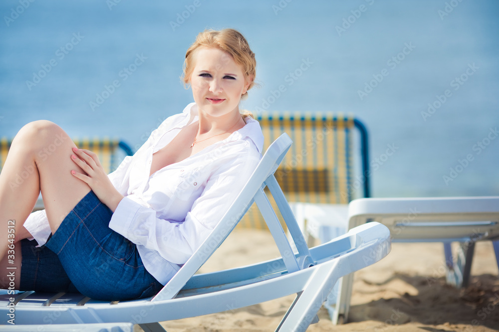 Beautiful woman sitting in chaise on the beach