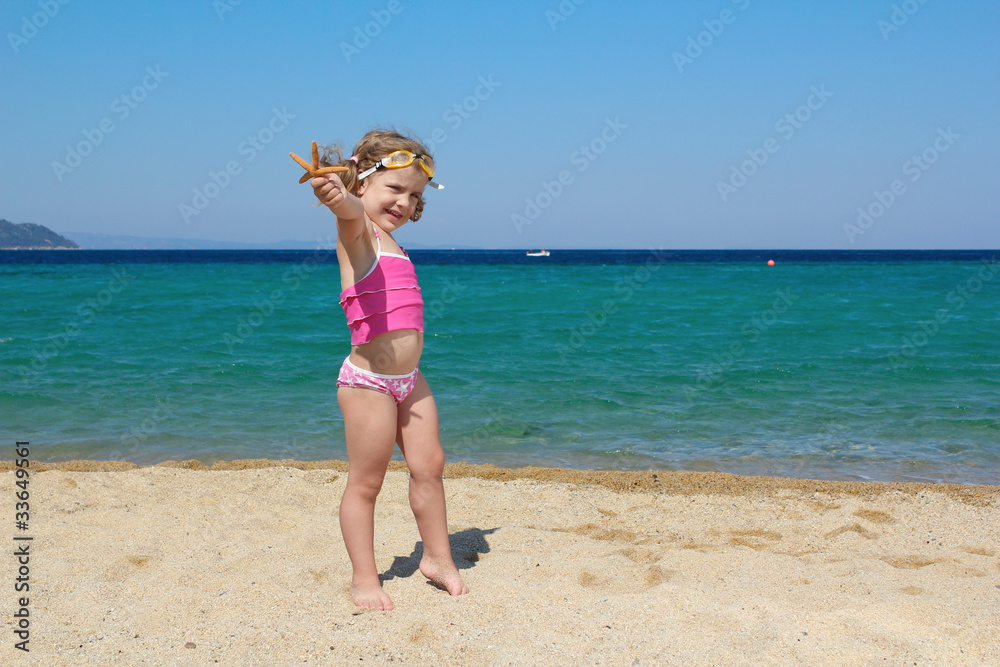 little girl with starfish and goggles on beach