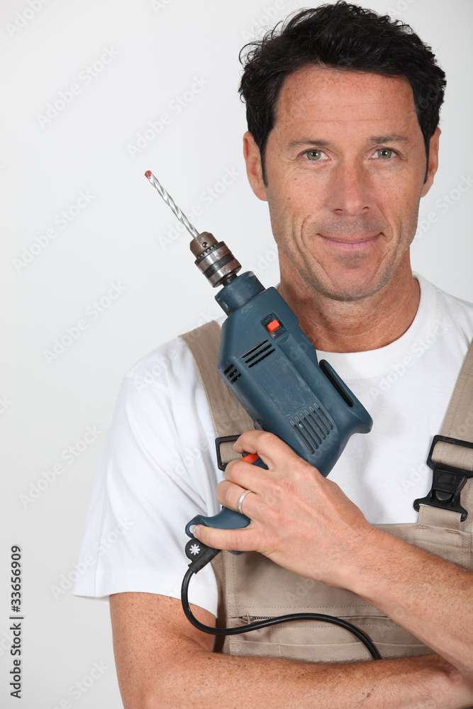A smiling man holding a hammer drill and looking at us.