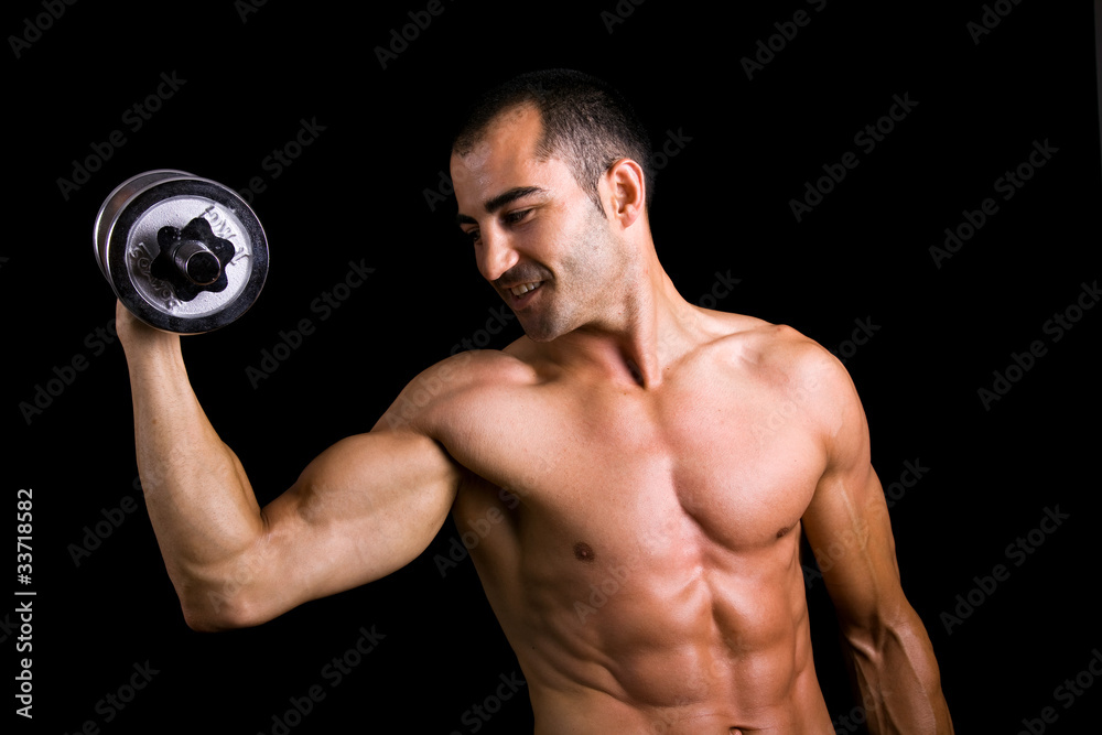 Young muscular man lifting dumbbells against black background