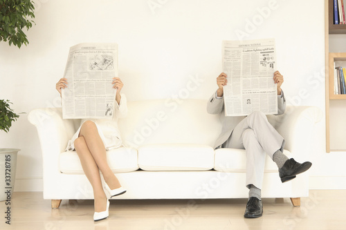 ソファーの両端で新聞を読む男女