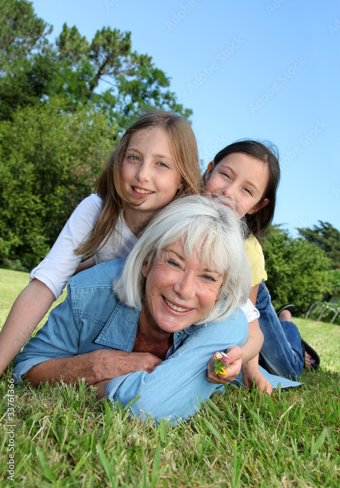 Senior woman lying down in park with girls on his back Senior woman lying down in park with girls on his back