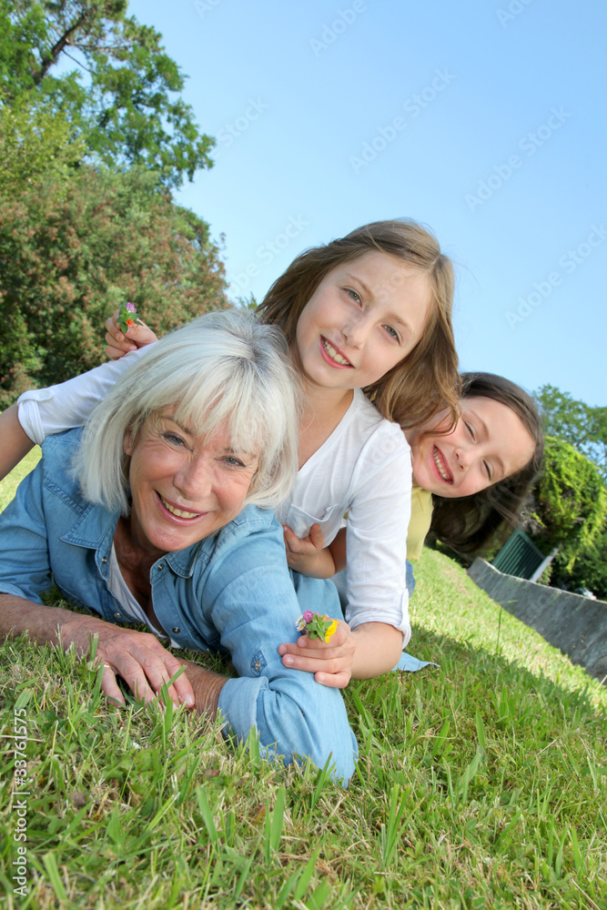 Senior woman lying down in park with girls on his back