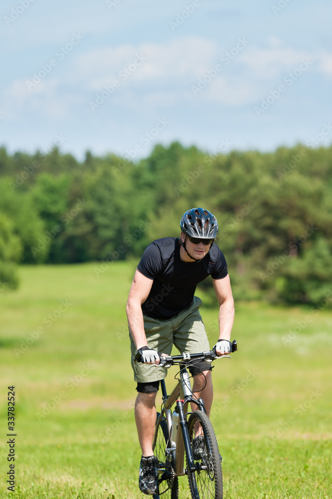 Sportive man mountain biking uphill sunny meadows