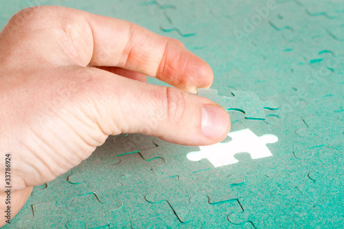 Hand inserting missing piece of green jigsaw puzzle into the hol
