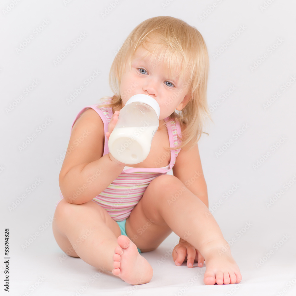 Adorable baby eating milk from the bottle sitting on white Adorable baby eating milk from the bottle sitting on white