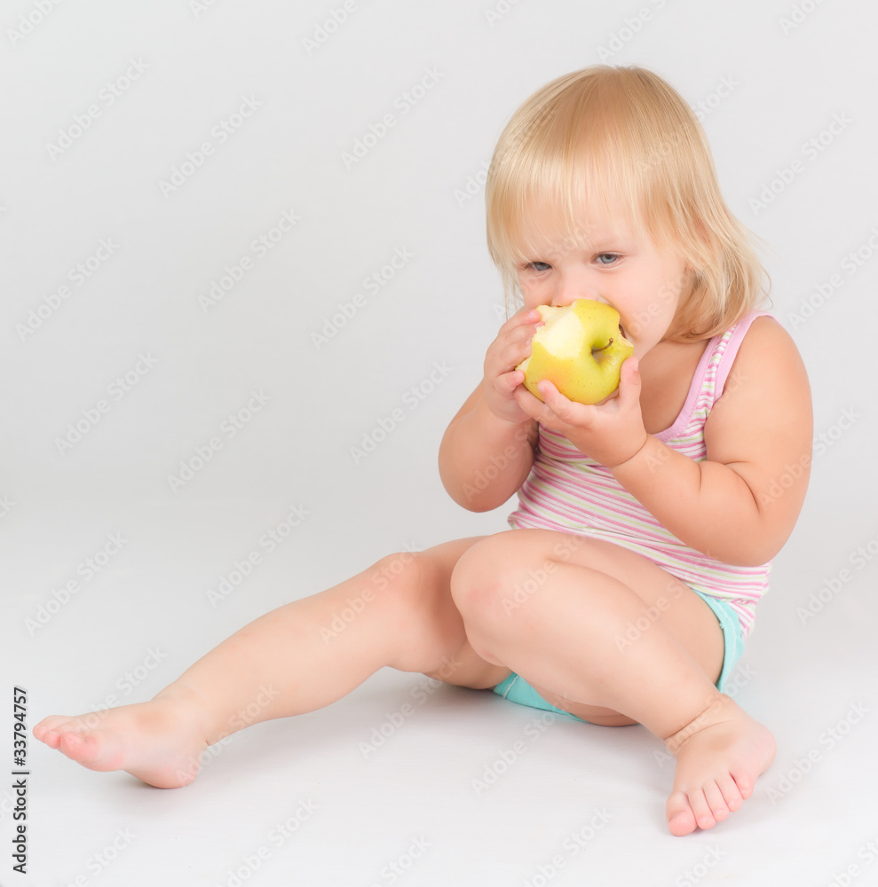 Adorable toddler girl eat green fresh apple sitting on white Adorable toddler girl eat green fresh apple sitting on white